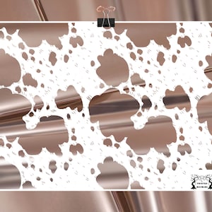 May include: A poster with a white cowhide pattern over a metallic rose gold background. The poster is held by a black clip. The Twisted Baubles logo is in the bottom right corner.