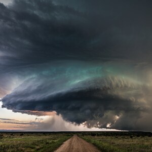 Puede incluir: Una gran nube de tormenta oscura y amenazante con un tono verde cuelga baja sobre un camino de tierra en un campo de hierba.