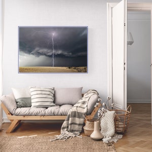 May include: A photograph of a lightning strike in a dark, stormy sky over a field of dry grass. The lightning bolt is white and bright, and the sky is dark and dramatic.