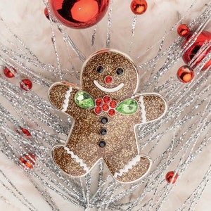 May include: A gingerbread man Christmas ornament with glitter, red and green jewels, and a white icing design.