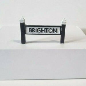 May include: A black and white sign with the word "BRIGHTON" printed on it. The sign is mounted on two black posts with white caps.