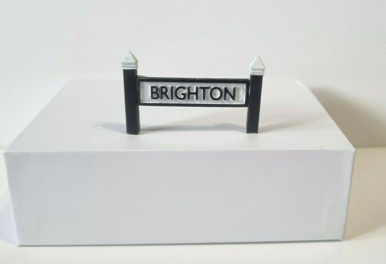 May include: A black and white sign with the word "BRIGHTON" printed on it. The sign is mounted on two black posts with white caps.
