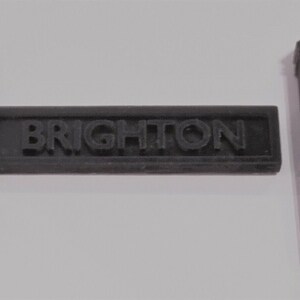 May include: A black plastic sign with the word "BRIGHTON" in raised letters, flanked by two black plastic posts.