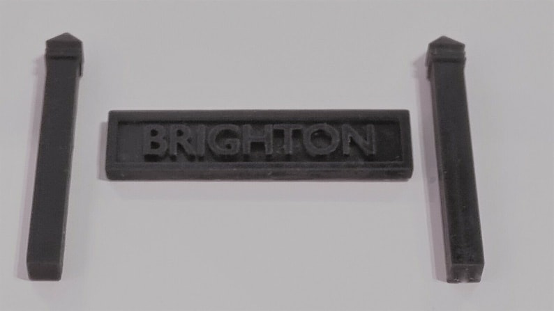 May include: A black plastic sign with the word "BRIGHTON" in raised letters, flanked by two black plastic posts.