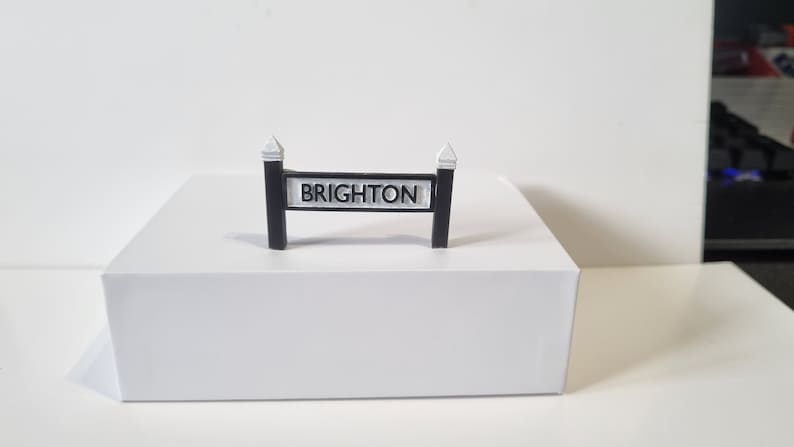 May include: A black and white sign with the word "BRIGHTON" printed on it. The sign is mounted on two black posts with white caps.