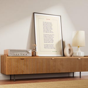 May include: A wooden media console with two doors and black metal legs. A vintage stereo receiver sits on top of the console. A framed print with the poem "Invictus" by William Ernest Henley is hanging on the wall above the console. A white ceramic lamp with a cream-colored shade sits on the console next to a beige ceramic sculpture.