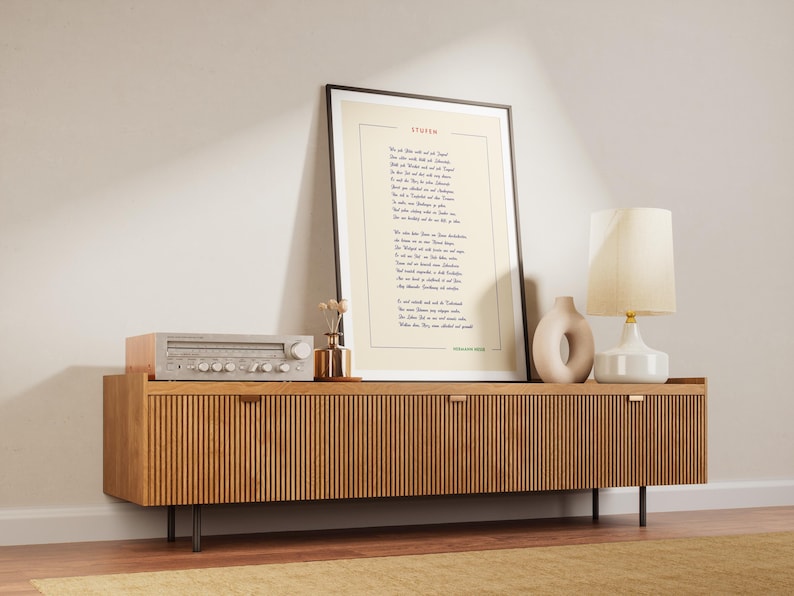 May include: A wooden media console with two doors and black metal legs. A vintage stereo receiver sits on top of the console. A framed print with the poem "Invictus" by William Ernest Henley is hanging on the wall above the console. A white ceramic lamp with a cream-colored shade sits on the console next to a beige ceramic sculpture.