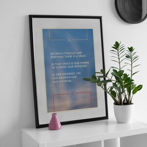 Pode incluir: Uma impress&atilde;o emoldurada com fundo azul e texto branco que diz "BETWEEN STIMULUS AND RESPONSE THERE IS A SPACE. IN THAT SPACE IS OUR POWER TO CHOOSE OUR RESPONSE. IN OUR RESPONSE LIES OUR GROWTH AND OUR FREEDOM." A impress&atilde;o est&aacute; em uma prateleira branca com um pequeno vaso rosa e uma planta em vaso.