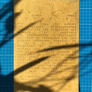 May include: A close-up of a piece of paper with handwritten text in Japanese. The paper is light brown and has a textured surface. The text is in black ink and is difficult to read.