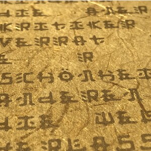 May include: Close-up of a textured, gold-coloured surface with black text. The text is in a foreign language and includes the word "SCH&Ouml;NE".
