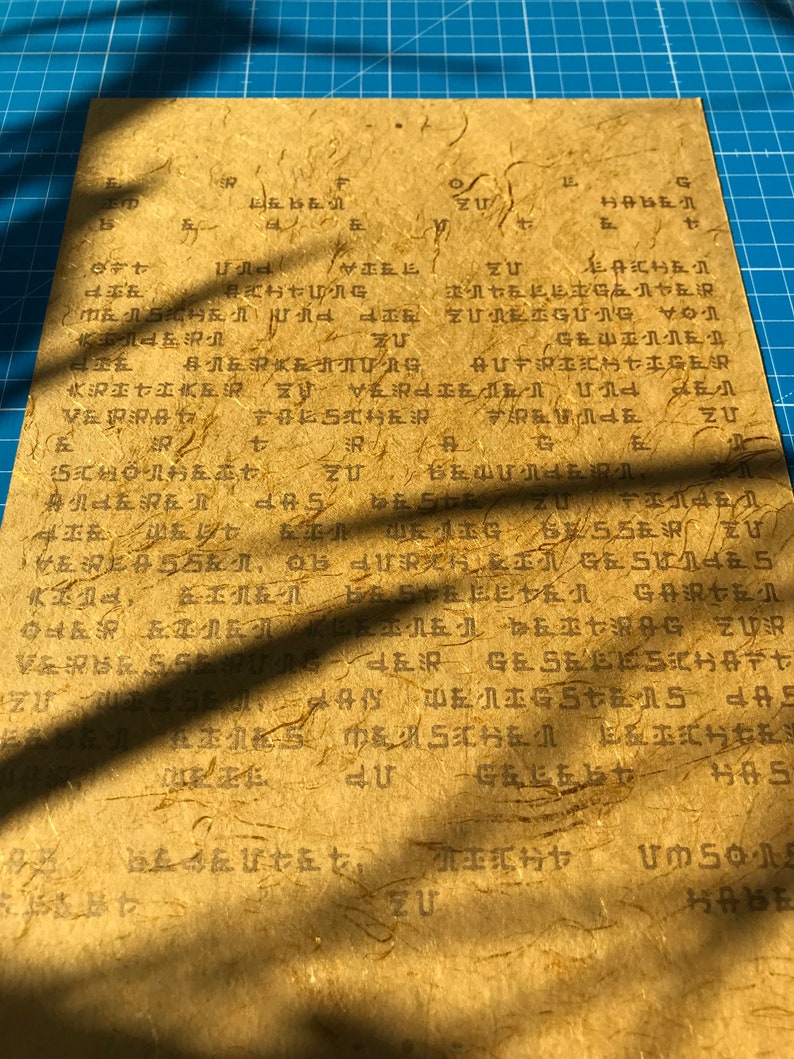 May include: A close-up of a piece of paper with Japanese text written on it. The paper is a light brown colour and has a rough texture. The text is written in black ink and is difficult to read.