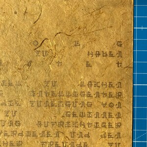 May include: A close-up of a piece of paper with handwritten text in black ink. The paper is textured and has a light brown colour. The text is in a cursive style and is difficult to read. The text includes the words "zu" and "g".