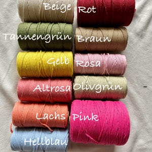 May include: An assortment of macrame cord spools in a range of colours, such as beige, red, green, brown, yellow, pink, orange, and blue. Each spool is labelled with its colour name in white text. The cords are tightly wound and ready for crafting projects.
