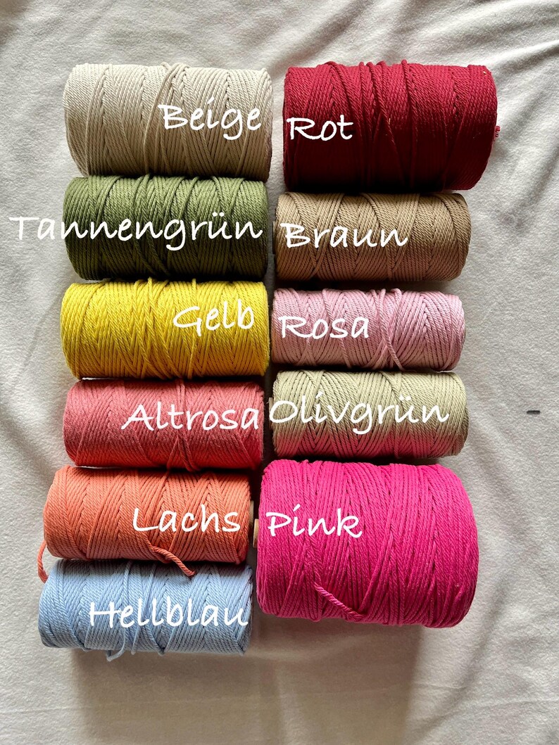 May include: An assortment of macrame cord spools in a range of colours, such as beige, red, green, brown, yellow, pink, orange, and blue. Each spool is labelled with its colour name in white text. The cords are tightly wound and ready for crafting projects.