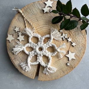 May include: A white crocheted snowflake ornament with fringe hanging on a wooden slice with small wooden stars scattered around it.