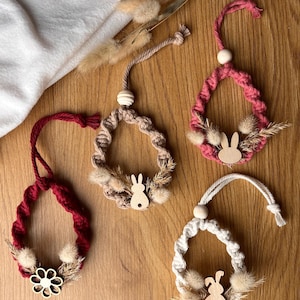 May include: Four handmade Easter decorations. Each features a woven ring in burgundy, pink, beige, and white. They are decorated with wooden bunny cutouts, dried grasses, and fluffy accents. The ornaments hang from knotted cords.