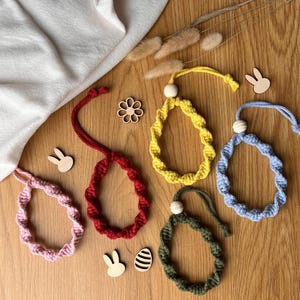 May include: A selection of colourful, handmade Easter egg decorations. The ornaments are in shades of pink, red, yellow, blue, and green, with a wooden bead and a loop for hanging. Wooden bunny and flower cutouts are scattered around.