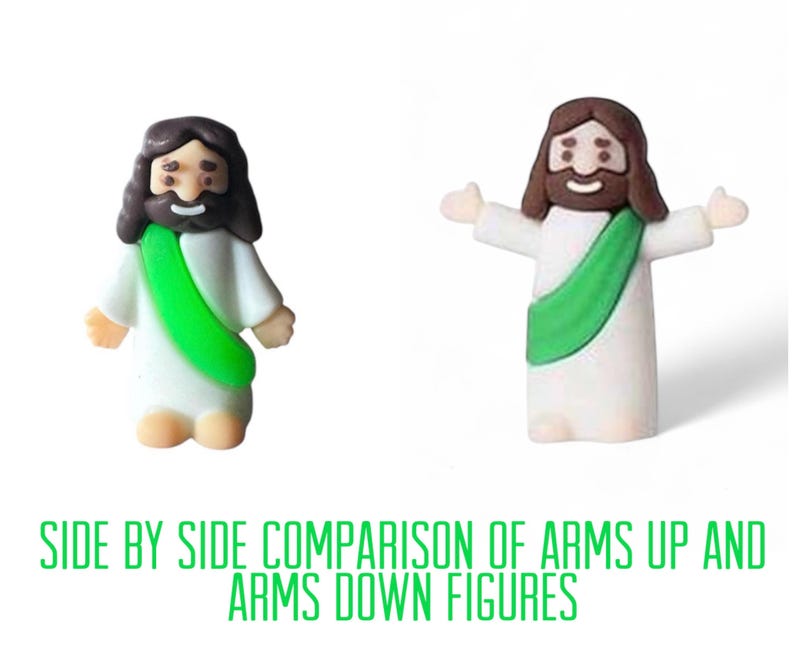 May include: Two small figurines of a religious figure, one with arms down and the other with arms up, are shown side by side. The figures have brown hair and beards, white robes, and green sashes. The text at the bottom reads "SIDE BY SIDE COMPARISON OF ARMS UP AND ARMS DOWN FIGURES."
