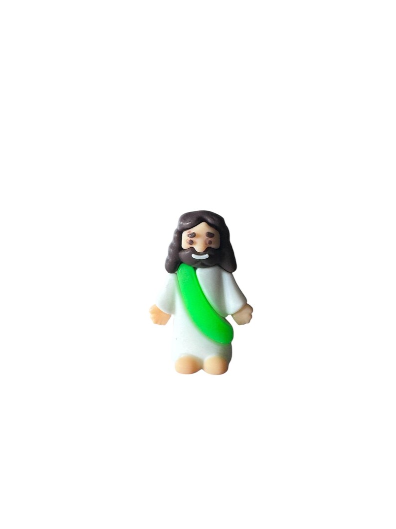 May include: A small, cartoon-style figurine of a religious figure. The figure has dark brown hair and a beard, wearing a white robe with a green sash. The figurine has a smiling expression and is standing.