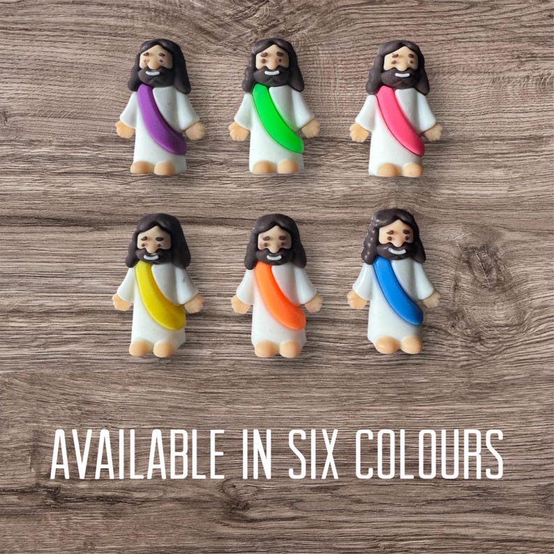 May include: Six small figurines of Jesus with different colored sashes: purple, green, pink, yellow, orange, and blue. The figurines have brown hair and beards, and are wearing white robes. The text "AVAILABLE IN SIX COLOURS" is at the bottom.