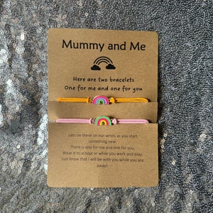 May include: A card with the text "Mummy and Me" and a rainbow graphic. The card is accompanied by two colorful bracelets with rainbow charms. The text on the card reads "Here are two bracelets, One for me and one for you. Lets tie these on our wrists as you start something new. There is one for me and one for you. Wear it to school or while you work and play. Just know that I will be with you while you are away!"
