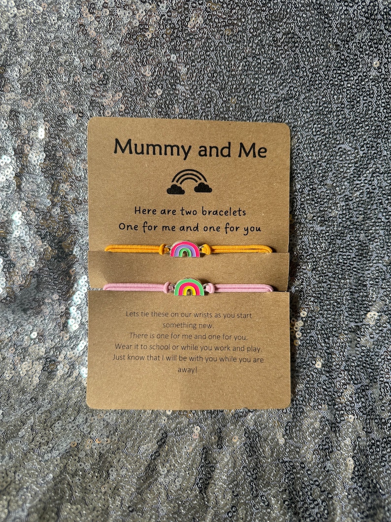 May include: A card with the text "Mummy and Me" and a rainbow graphic. The card is accompanied by two colorful bracelets with rainbow charms. The text on the card reads "Here are two bracelets, One for me and one for you. Lets tie these on our wrists as you start something new. There is one for me and one for you. Wear it to school or while you work and play. Just know that I will be with you while you are away!"
