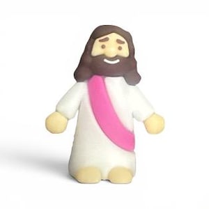 May include: A small, cartoon-like figurine of a religious figure. The figure has a white robe, a pink sash, and brown hair and beard. The figure's arms and feet are a light tan color. The figure is smiling.
