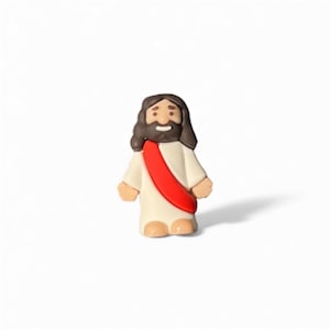 May include: A small figurine of Jesus Christ, depicted with brown hair and a beard, wearing a white robe and a red sash. The figure has a smiling expression and is standing upright. The figurine is on a white background.