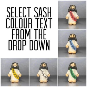 May include: A collection of small figurines of Jesus wearing a white robe and a sash with the text "Jesus ❤️ You". The sash colors include red, blue, yellow, and green. The image also includes the text "SELECT SASH COLOUR TEXT FROM THE DROP DOWN".
