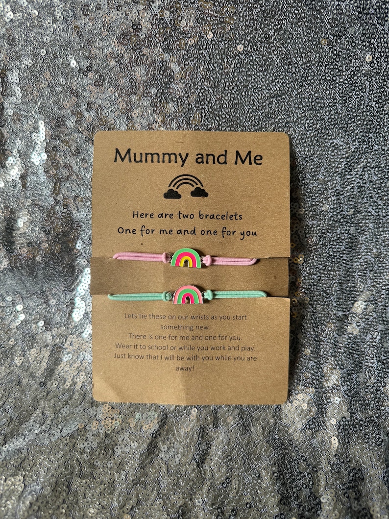 May include: A card with the text "Mummy and Me" and a rainbow graphic. The card says "Here are two bracelets, one for me and one for you."  The card also includes a message about tying the bracelets on wrists and wearing them to school or work.