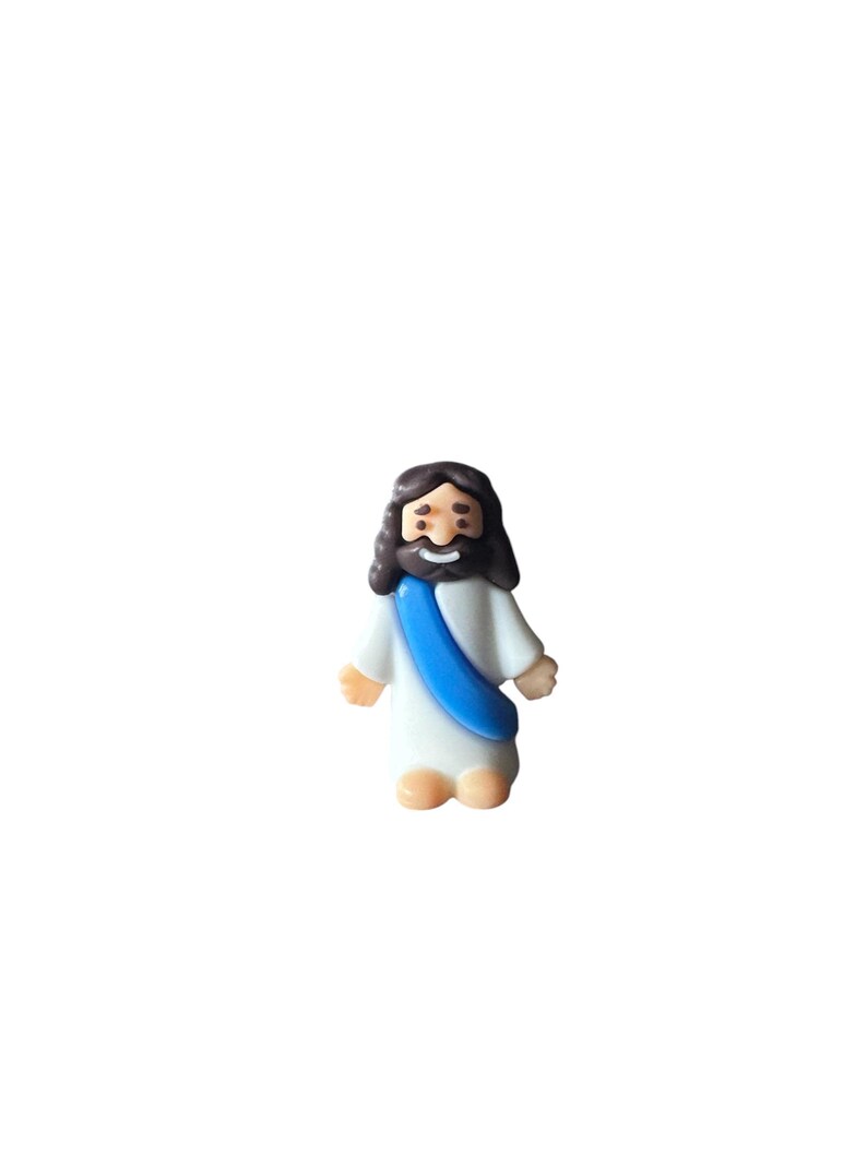 May include: A small figurine of Jesus Christ, depicted with dark brown hair and a beard. He wears a white robe with a blue sash. The figurine has a smiling expression and is standing upright.