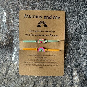 May include: A card with the text "Mummy and Me" and a rainbow design. The card is accompanied by two bracelets with rainbow charms. The text on the card reads "Here are two bracelets, One for me and one for you. Let's tie these on our wrists as you start something new. There is one for me and one for you. Wear it to school or while you work and play. Just know that I will be with you while you are away!"