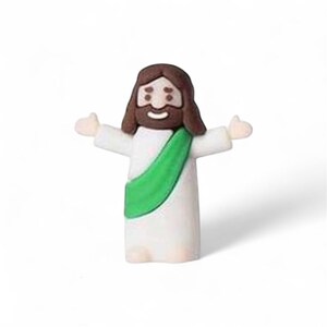 May include: A small figurine of Jesus with outstretched arms. The figure has brown hair and a beard, a white robe, and a green sash. The figurine is smiling and has a light skin tone.