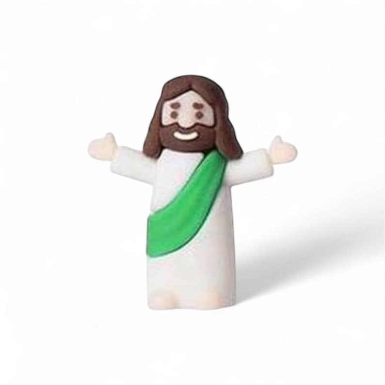 May include: A small figurine of Jesus with outstretched arms. The figure has brown hair and a beard, a white robe, and a green sash. The figurine is smiling and has a light skin tone.