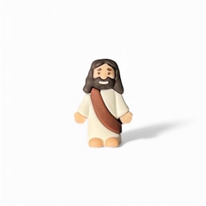 May include: A small, figurine of Jesus Christ, depicted with brown hair and a beard, wearing a white robe and a brown sash. The figure has a smiling expression and is standing on a white surface.