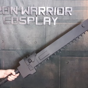 May include: A black, plastic, saw-toothed sword with a handle. The sword is held by a person's hand. The text "IRON-WARRIOR COSPLAY" is visible in the background.