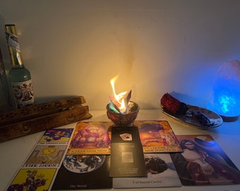 May include: A tarot card reading spread with a lit candle in a bowl, a salt lamp, and incense burning on a wooden surface. The cards are spread out in a circle and include "The Moon", "The World", "A Year From Now", "Choose a New Direction", "5 of Sacred Circles", and "Princess of Cups".