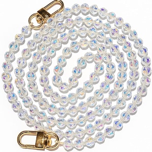 Peut inclure: Une chaîne de perles transparente et irisée avec des fermoirs dorés. La chaîne est composée de plusieurs brins de perles transparentes et facettées, créant un effet scintillant. Les fermoirs sont de conception simple et sûre.