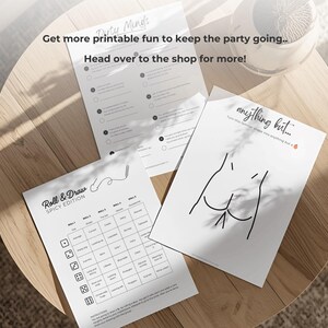 May include: Three white printed sheets with party game prompts and illustrations are arranged on a wooden table. The text on the sheets includes "Dirty Minds", "Roll & Draw SPICY EDITION", and "anything but...".
