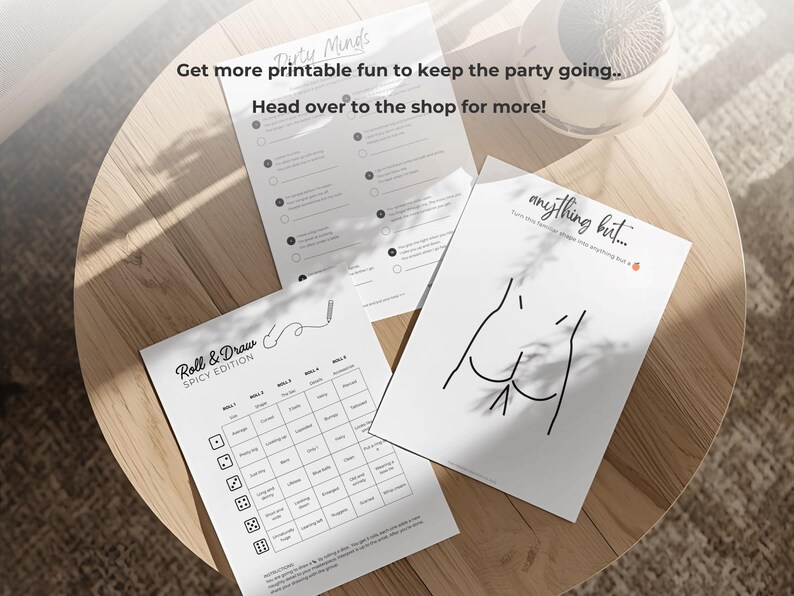 May include: Three white printed sheets with party game prompts and illustrations are arranged on a wooden table. The text on the sheets includes "Dirty Minds", "Roll & Draw SPICY EDITION", and "anything but...".