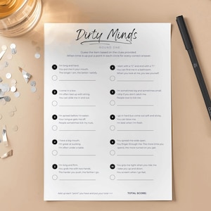 May include: A printed game sheet titled "Dirty Minds" with fill-in-the-blank clues, a black pen, and scattered confetti. The game sheet is on a light beige surface, with a glass of liquid visible in the upper left corner.