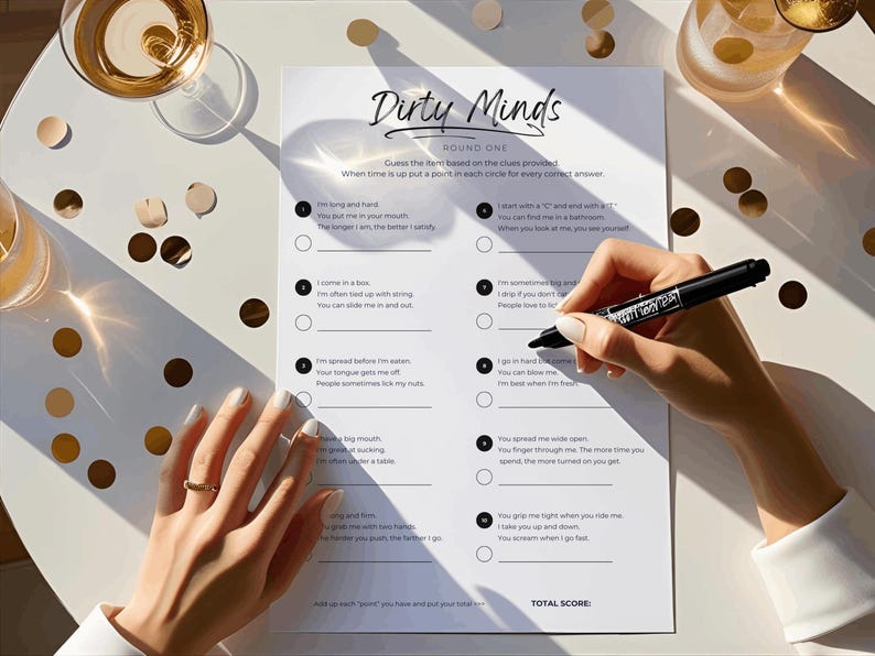 May include: A game of "Dirty Minds" is displayed on a white sheet of paper. The game sheet is on a white table, with a person's hand holding a black marker, ready to fill in the answers. Gold confetti and glasses of champagne are also on the table.