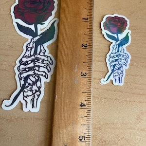 Skeleton hand with a red rose sticker.