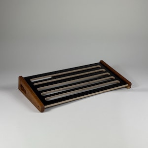 Puede incluir: Pedalera negra con lados de madera y cinco ranuras para pedales. La pedalera está hecha de madera contrachapada y tiene un acabado negro.