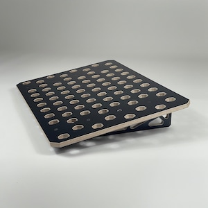 Może przedstawiać: Czarny drewniany stojak z siatką sześciokątnych otworów. Stojak jest pochylony i ma czarne metalowe podparcie.