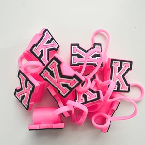 May include: A pile of pink silicone phone ring holders with a black and white letter "K" on each.
