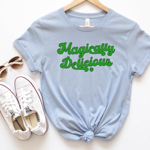 May include: A light blue t-shirt with the text "Magically Delicious" in green with shamrock symbols.