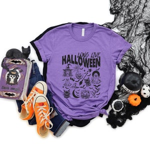 May include: Purple t-shirt with a black graphic that says "Long Live Halloween" and features a variety of Halloween-themed illustrations, including a witch, ghosts, bats, and a crescent moon.