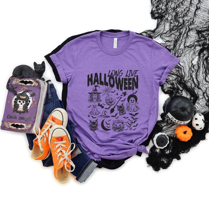 May include: Purple t-shirt with a black graphic that says "Long Live Halloween" and features a variety of Halloween-themed illustrations, including a witch, ghosts, bats, and a crescent moon.