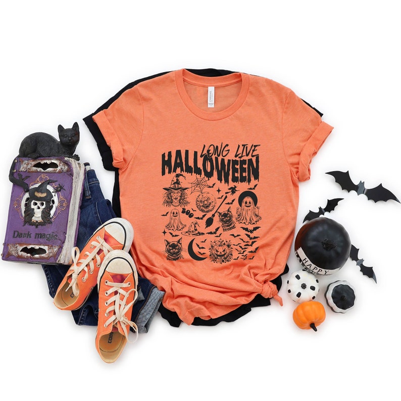 May include: Orange t-shirt with black text that reads "Long Live Halloween". The shirt features a graphic of various Halloween icons, including a witch, ghosts, bats, a cat, a crescent moon, and a pumpkin.